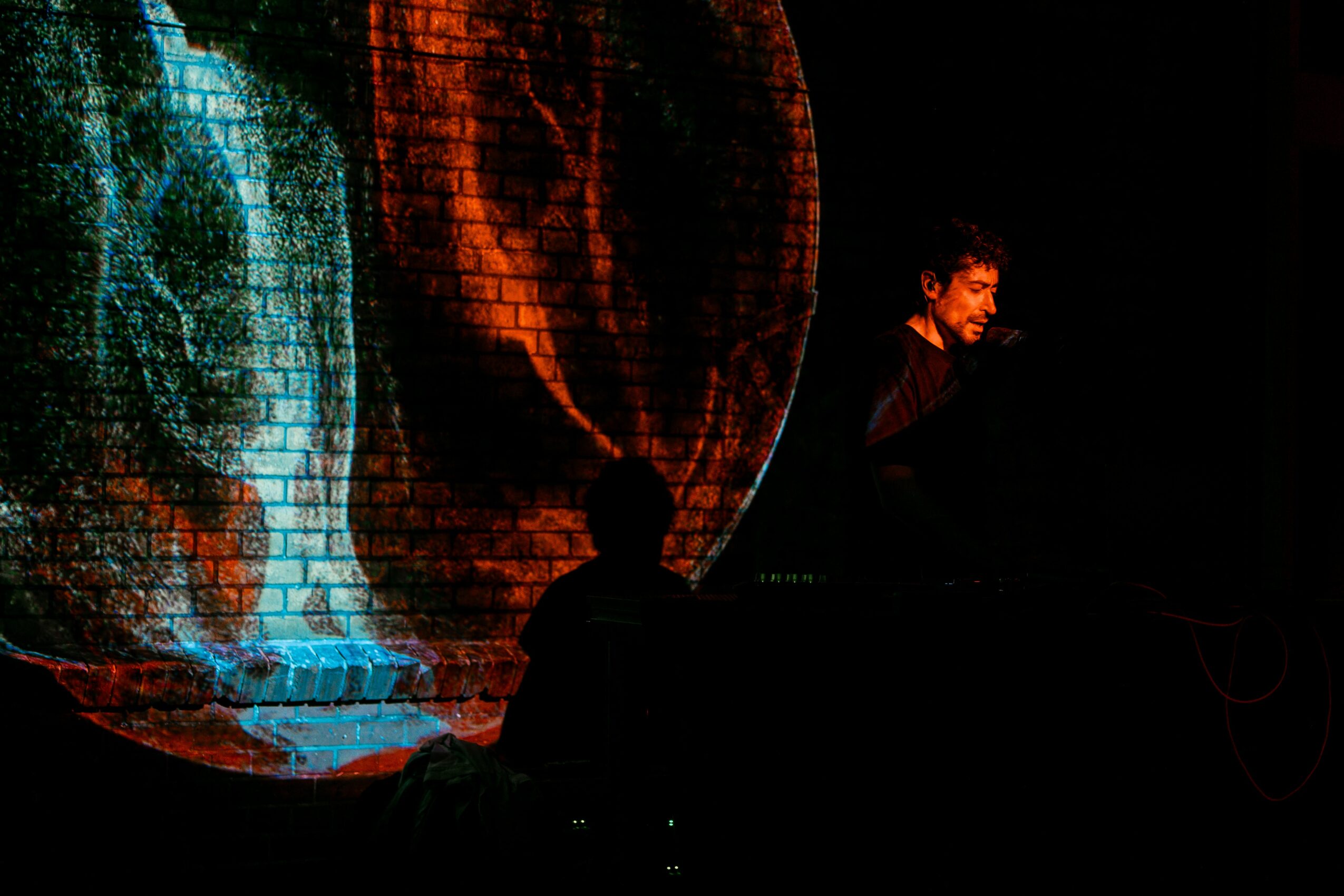 Person standing near a large, illuminated circular screen displaying colorful abstract patterns, in a dark environment.