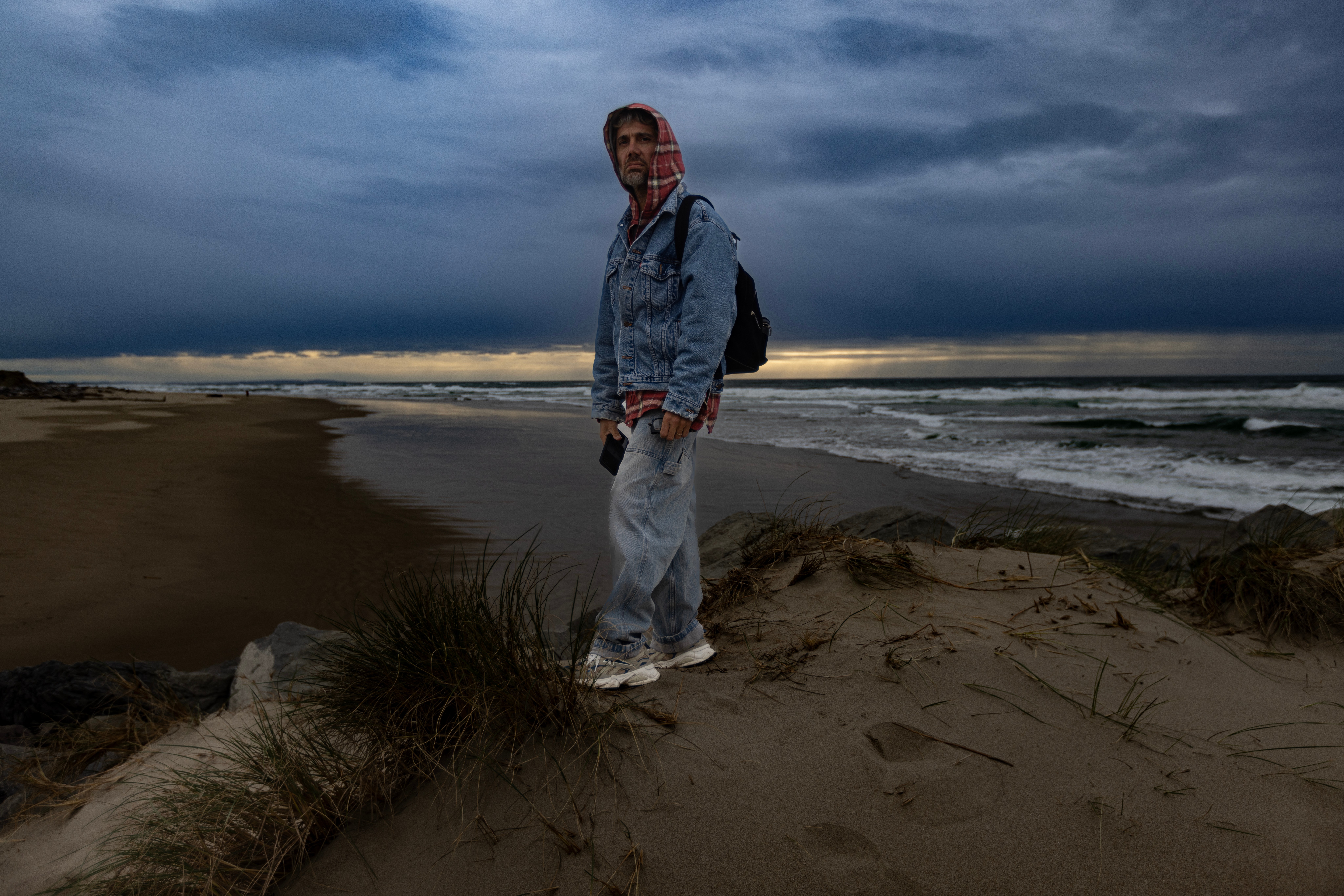 Person standing on a sandy beach with ocean waves and dark cloudy sky in the background.