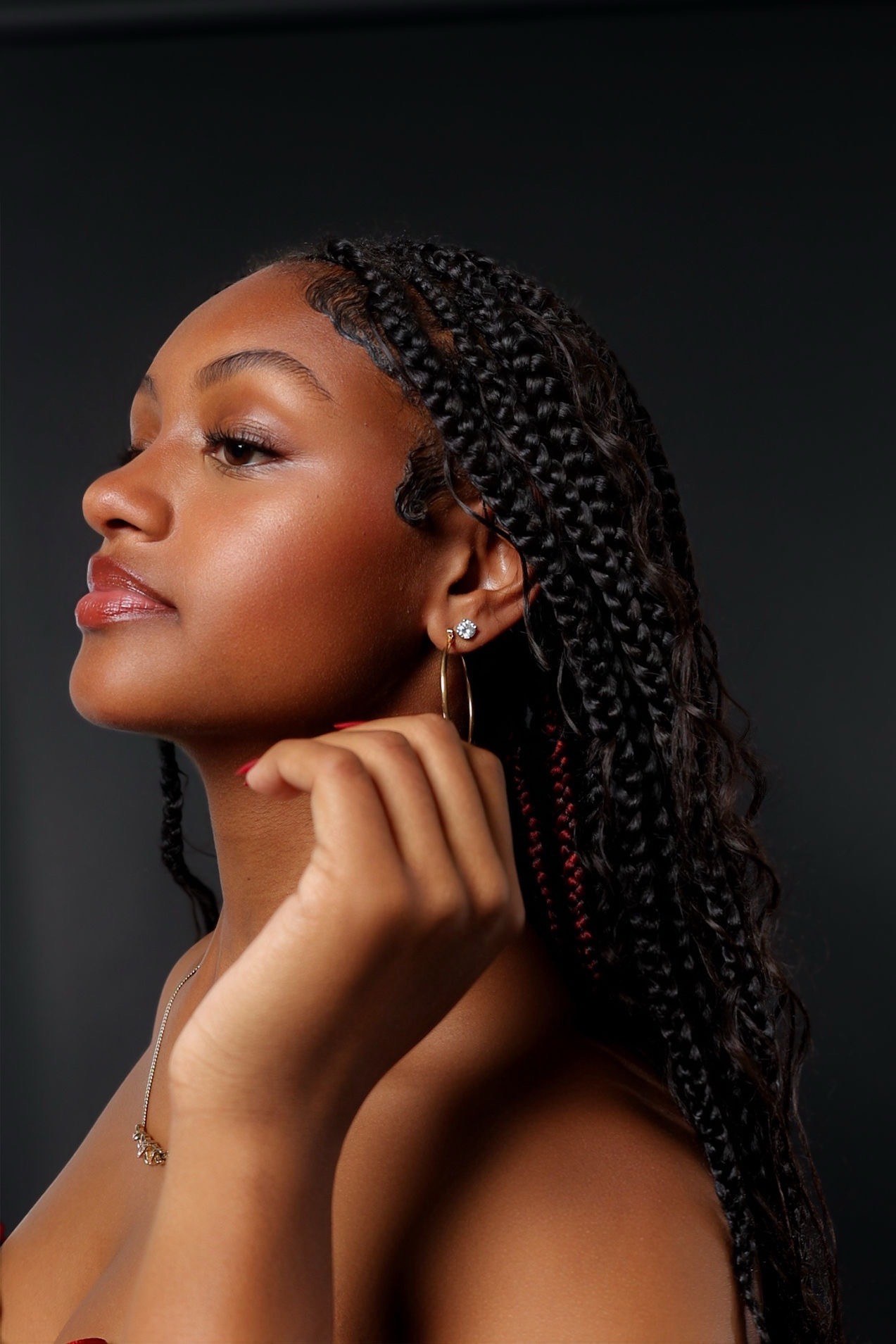 Side profile of a woman with braided hair, wearing a hoop earring, against a dark background.