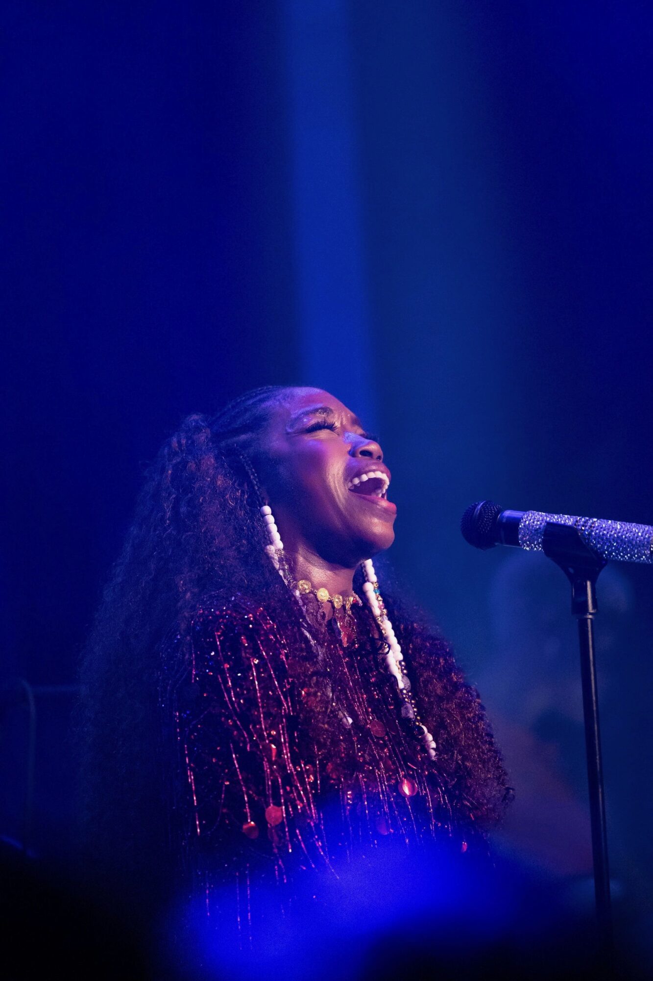 A woman singing passionately on stage with a microphone, illuminated by blue stage lighting.