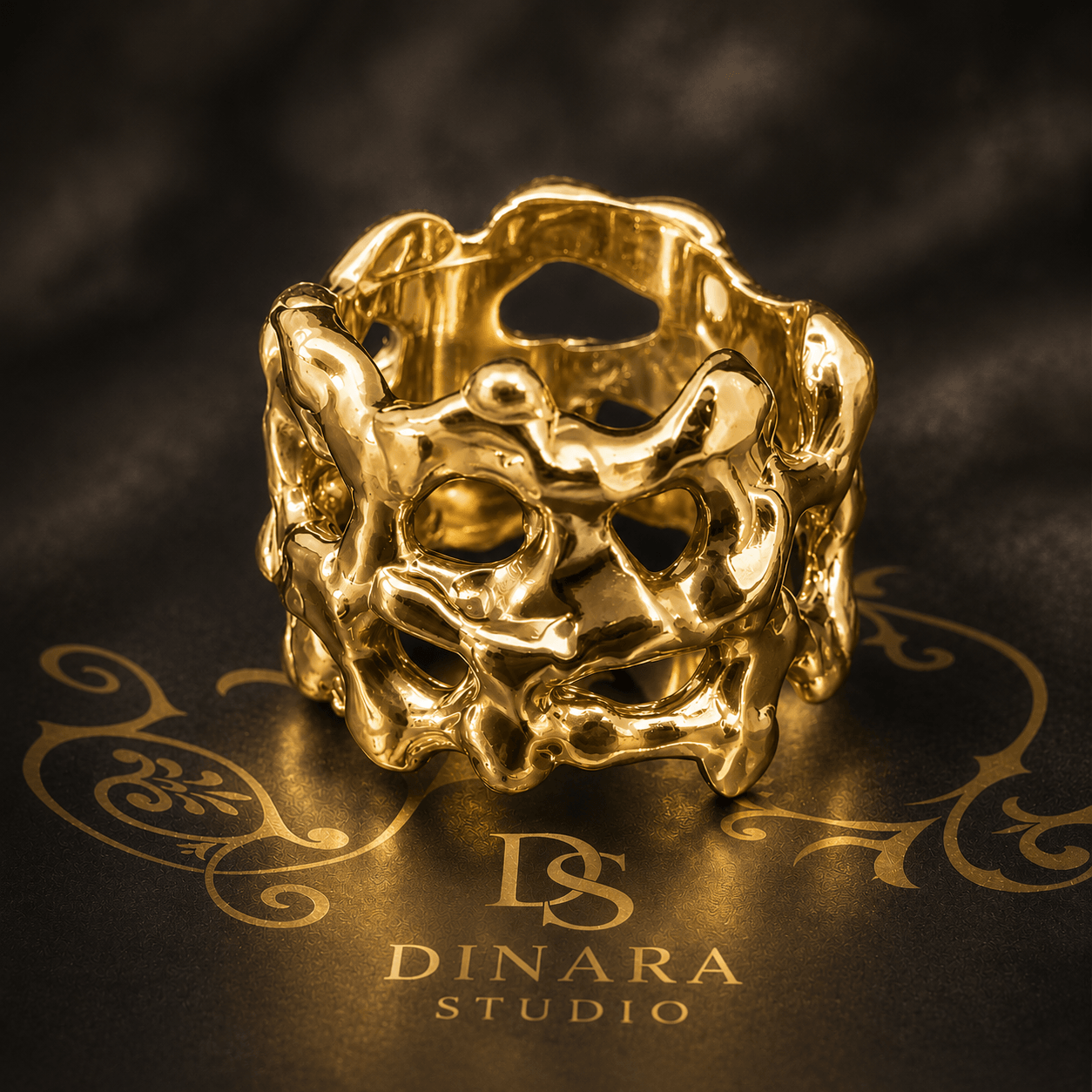 Gold ring with an intricate, abstract design, placed on a black surface with gold lettering and logo, studio background.