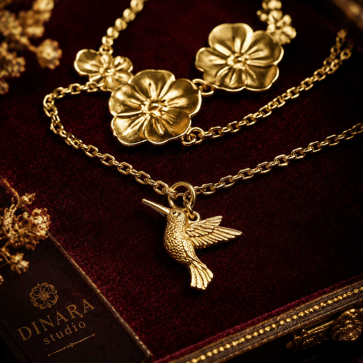 Gold necklace with flower and hummingbird pendants on dark fabric background.