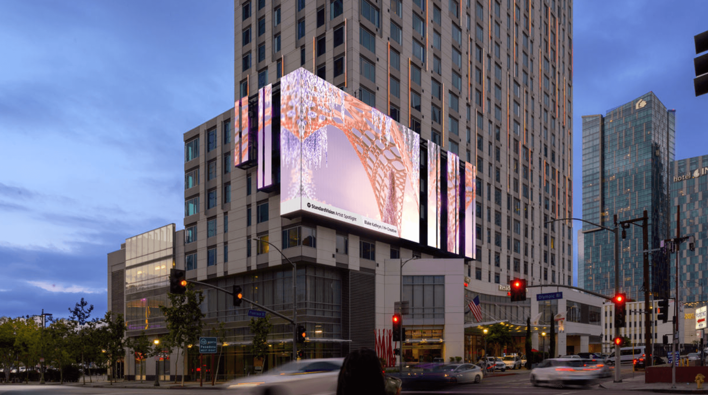 Large digital billboard on a tall building displays colorful abstract visuals, with city skyscrapers and traffic lights nearby.