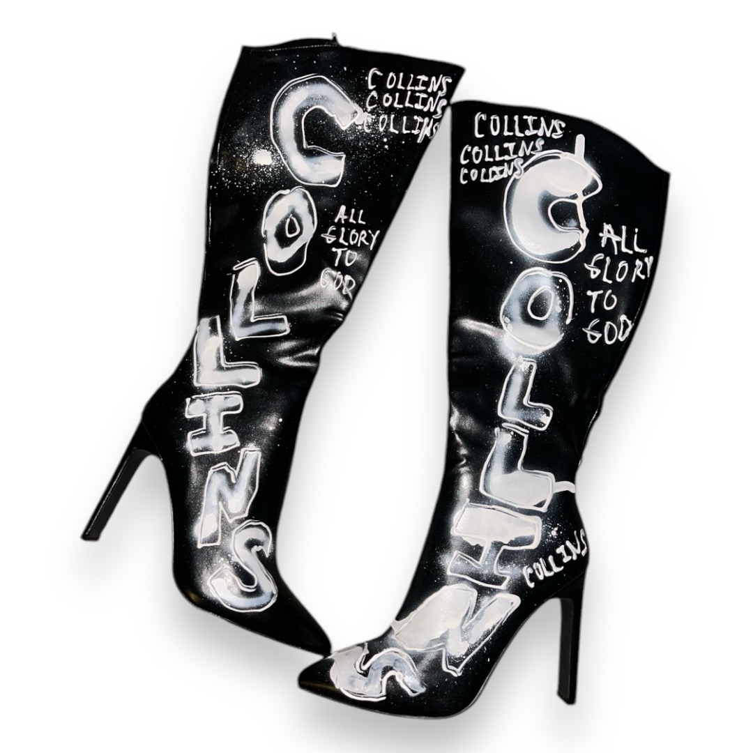 Pair of black high-heeled boots with white graffiti-style text and designs, including the word 'GOLLE' and phrases like 'ALL GLORY TO GOD'.