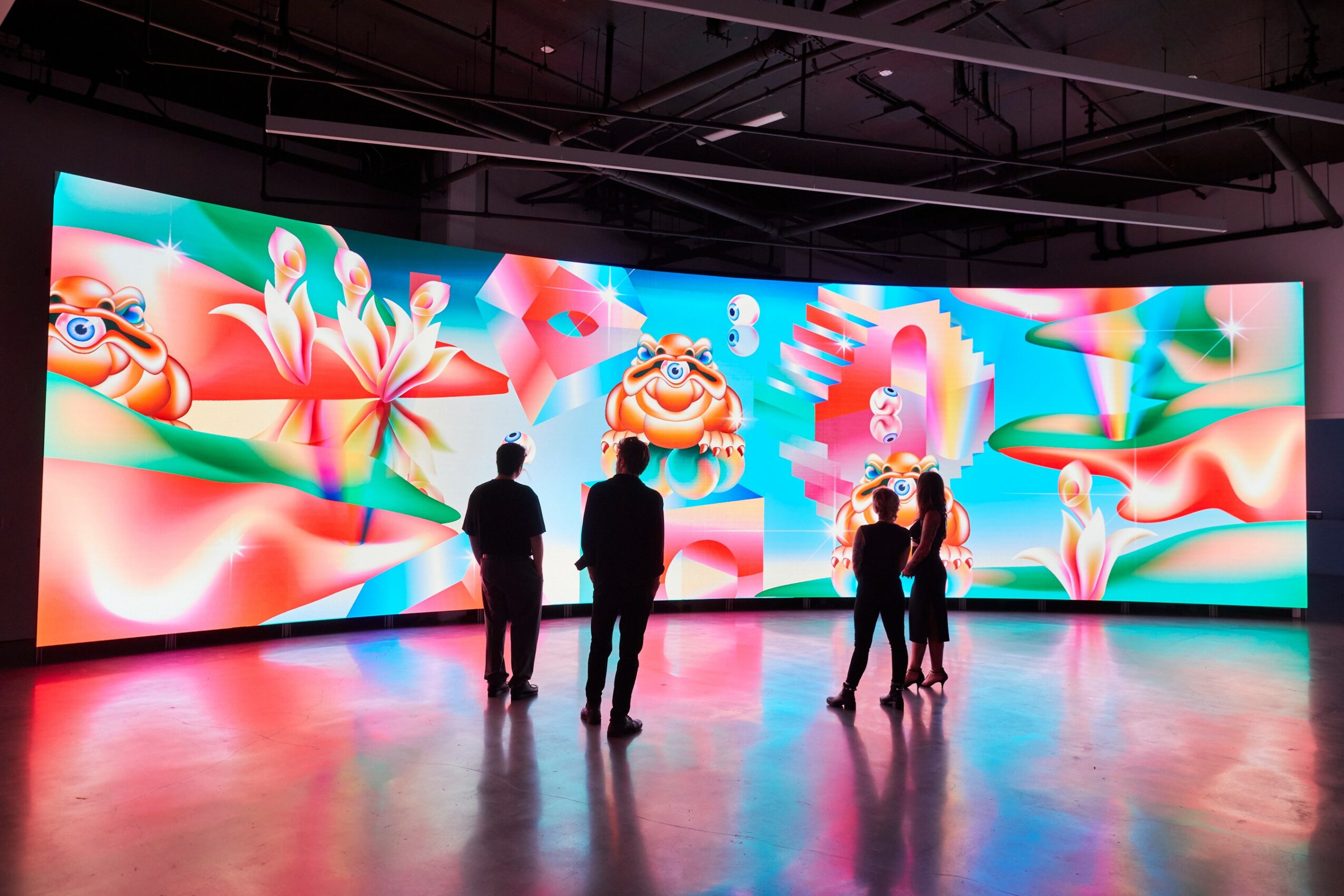 Group of five people standing in front of a large, colorful digital display with animated characters and abstract shapes.