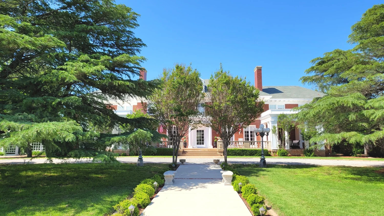 Pathway leading to a large building with trees and greenery on both sides, under a clear blue sky.