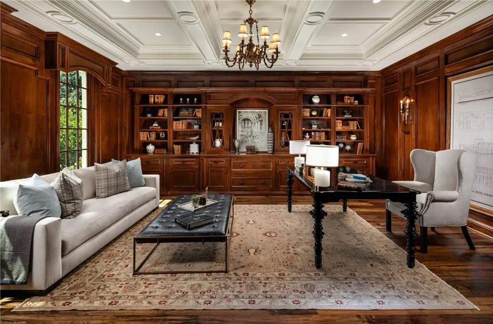 Elegant library room with wooden bookshelves, a chandelier, a sofa, a coffee table, and a desk with chairs.