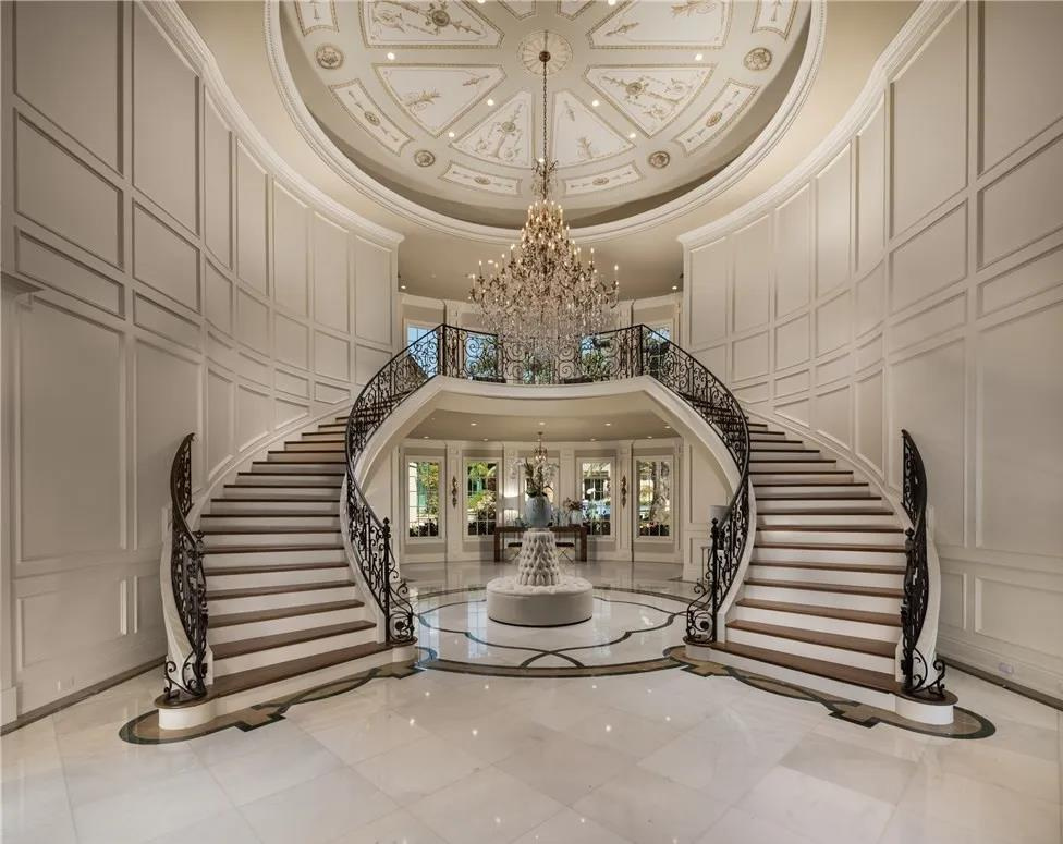 Elegant staircase with a chandelier in a grand interior, symmetrical design, curved stairs with ornate railings, marble floor, and high ceiling.