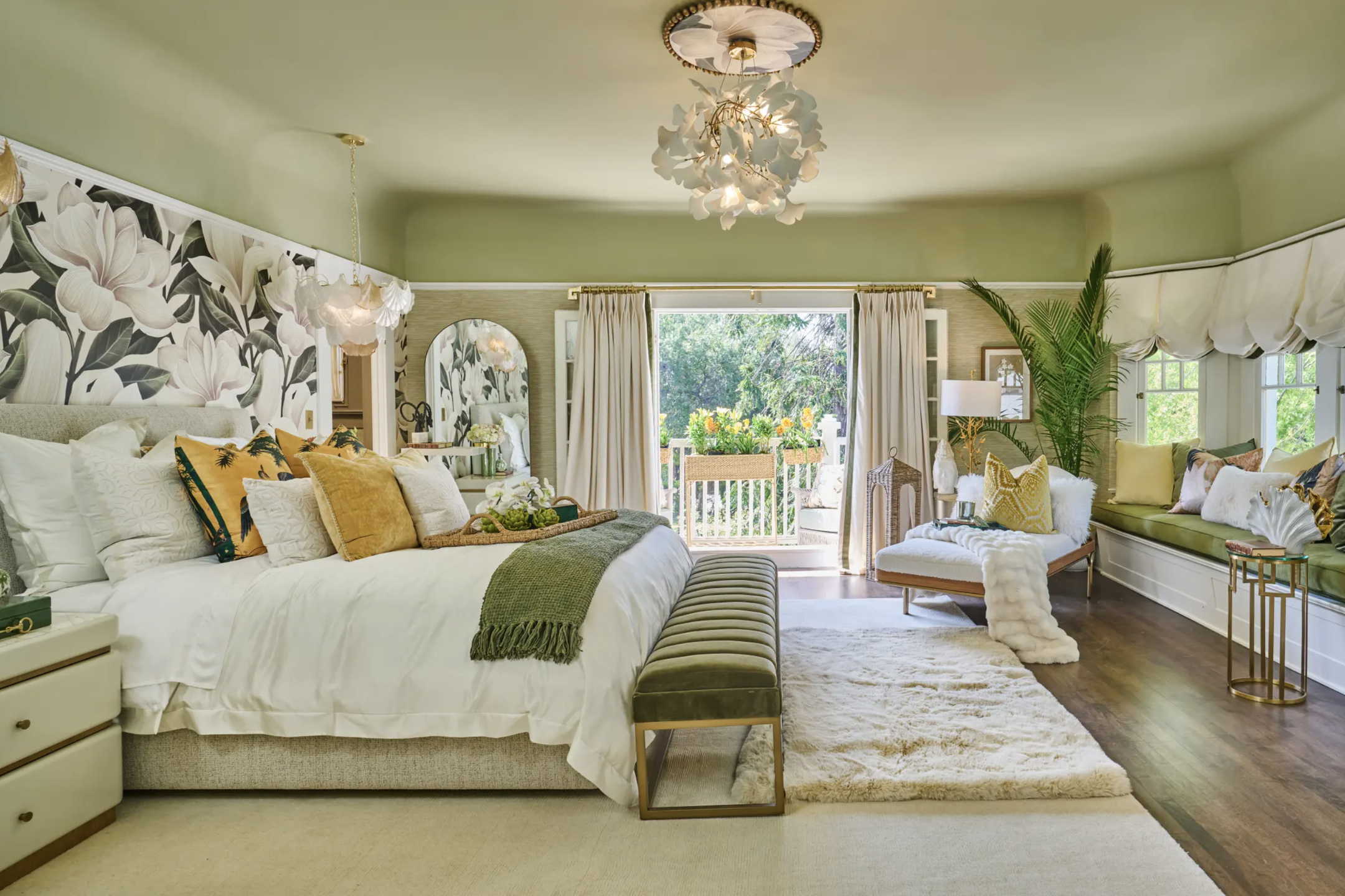 Bedroom with large bed, window seat, chandelier, and sliding glass door leading outside, decorated in light green and white tones.