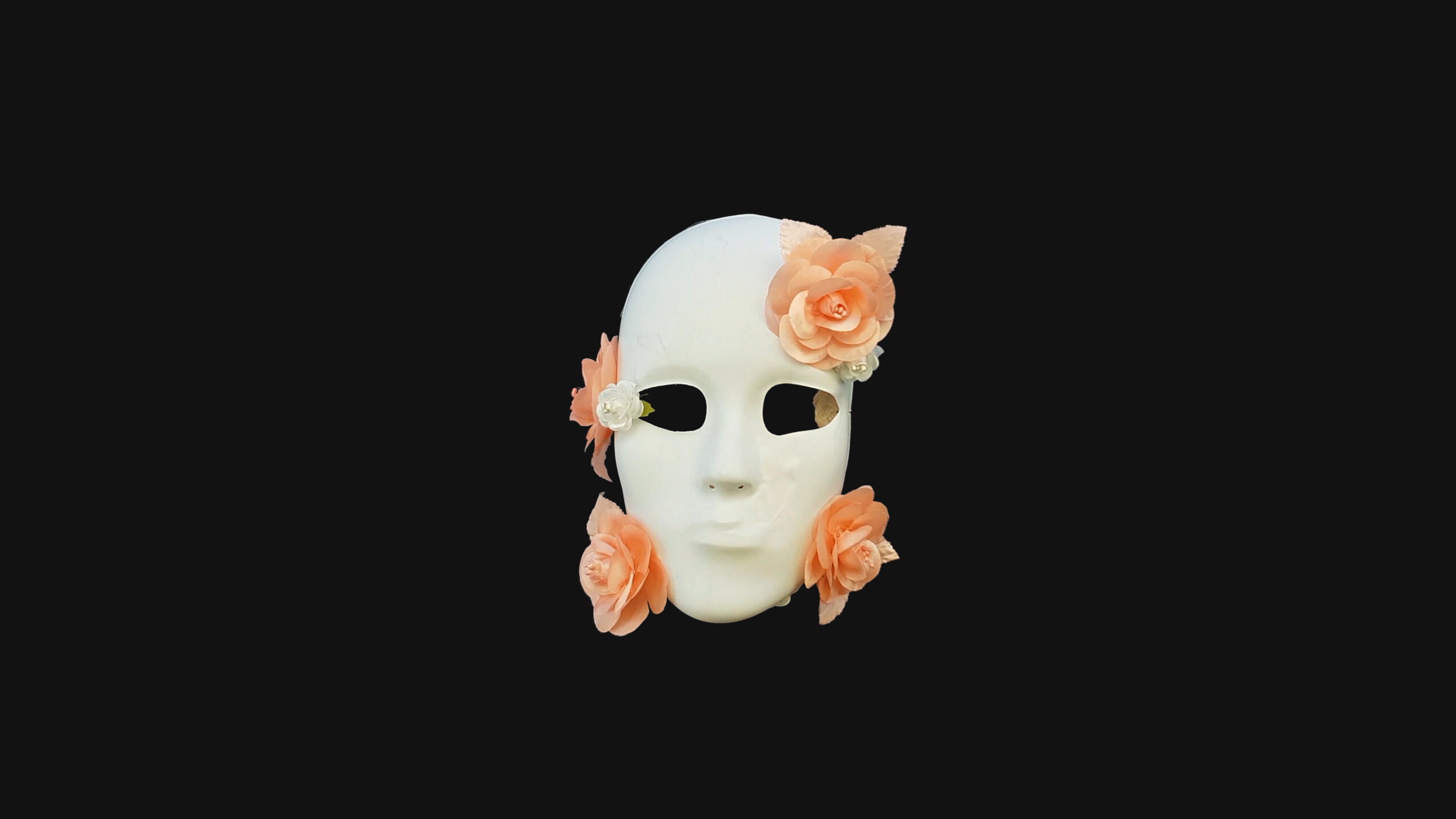 White mask with black eye holes decorated with peach-colored flowers, set against a black background.