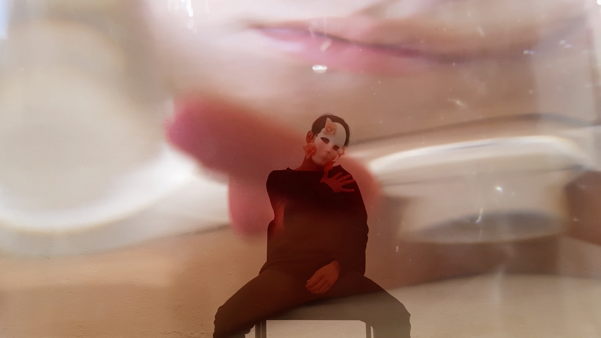 Person sitting with legs crossed, reflected in a glass surface, with a blurred face in the background.