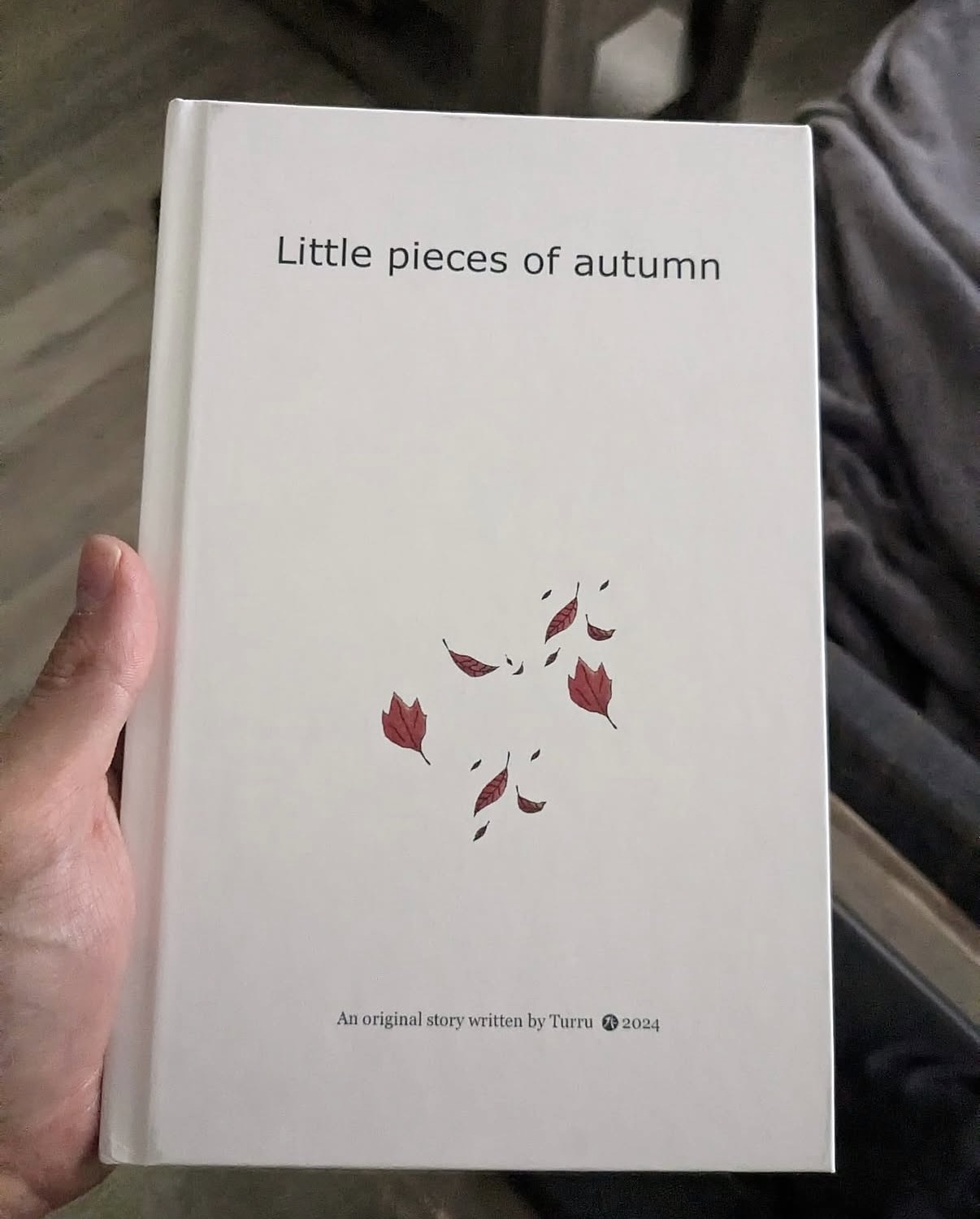Book titled 'Little pieces of autumn' with a white cover and red leaf illustrations, held in a person's hand.