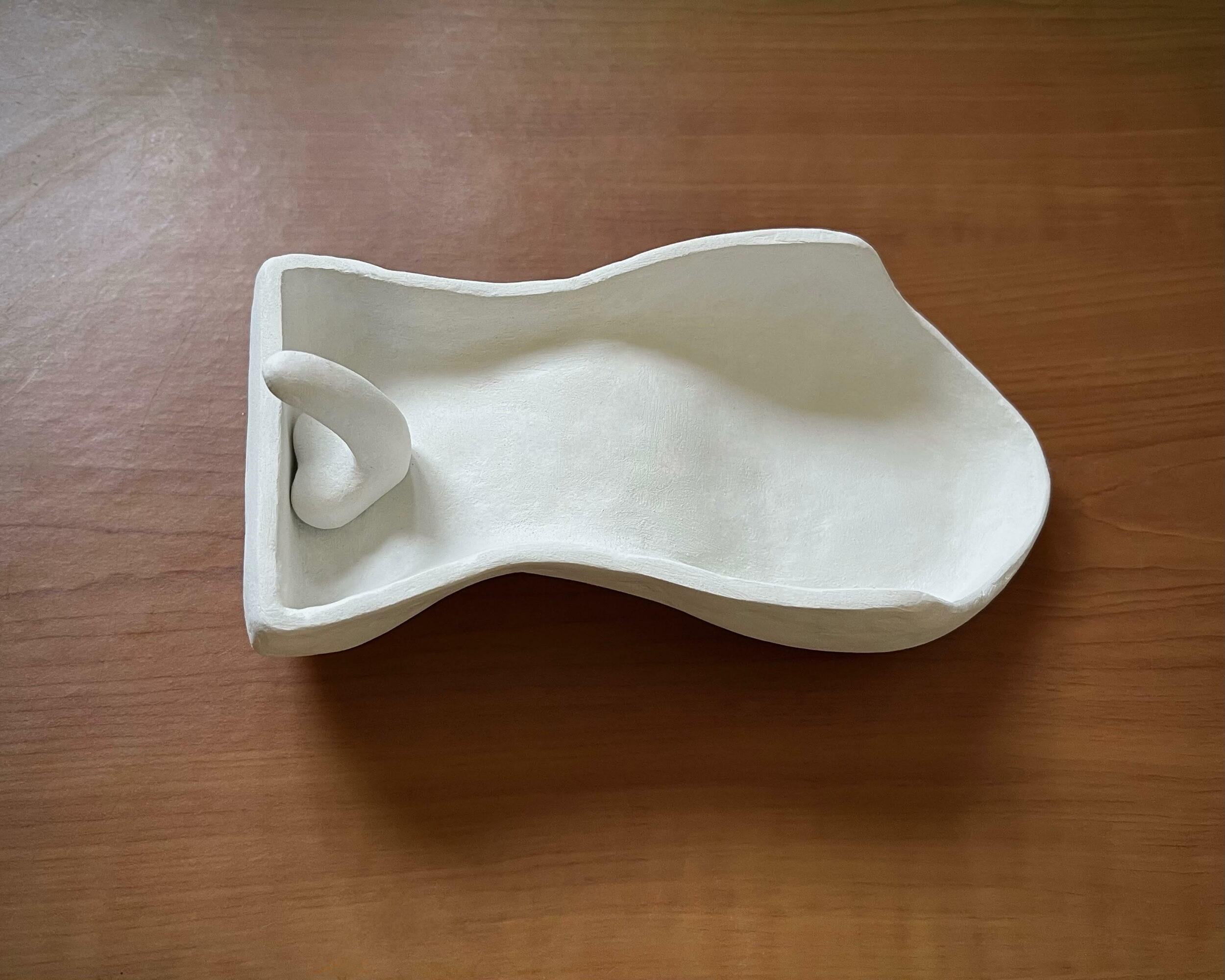 White ceramic soap dish with a curved design on a wooden surface.