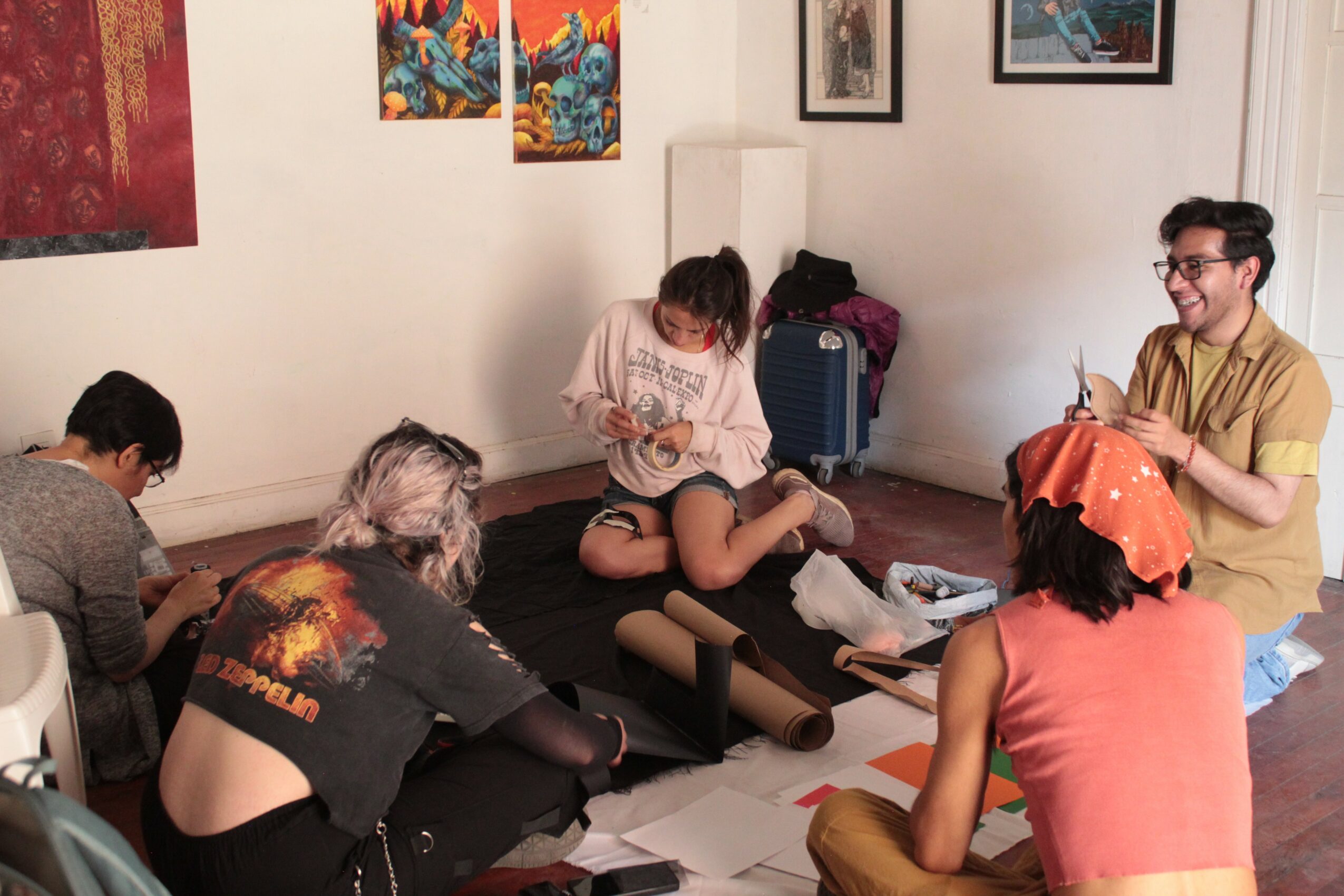 Group of five people sitting on the floor in an art studio, working on art projects with paintings on the wall behind them.
