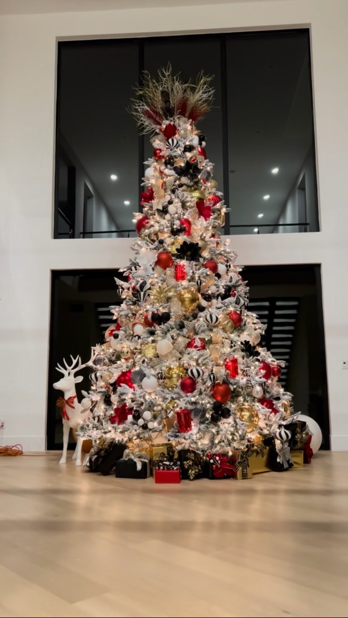 Decorated Christmas tree with red, gold, and white ornaments, surrounded by wrapped presents, in a modern indoor setting.