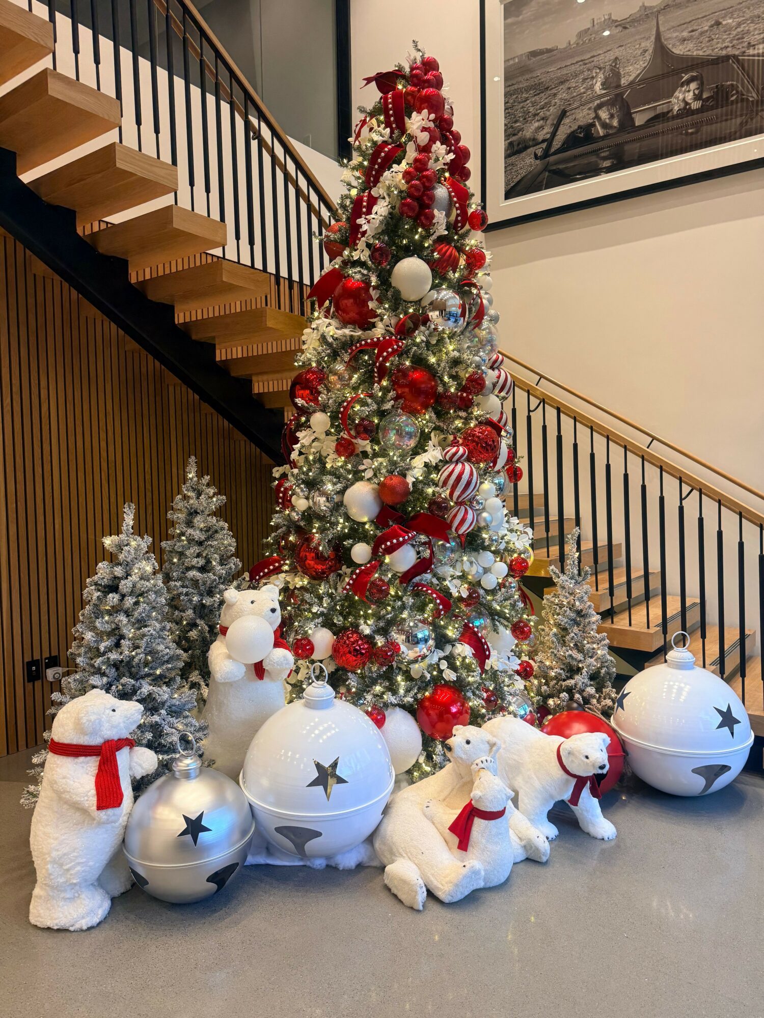 Decorated Christmas tree with red, white, and silver ornaments, surrounded by plush snowmen and silver trees, on a gray floor.