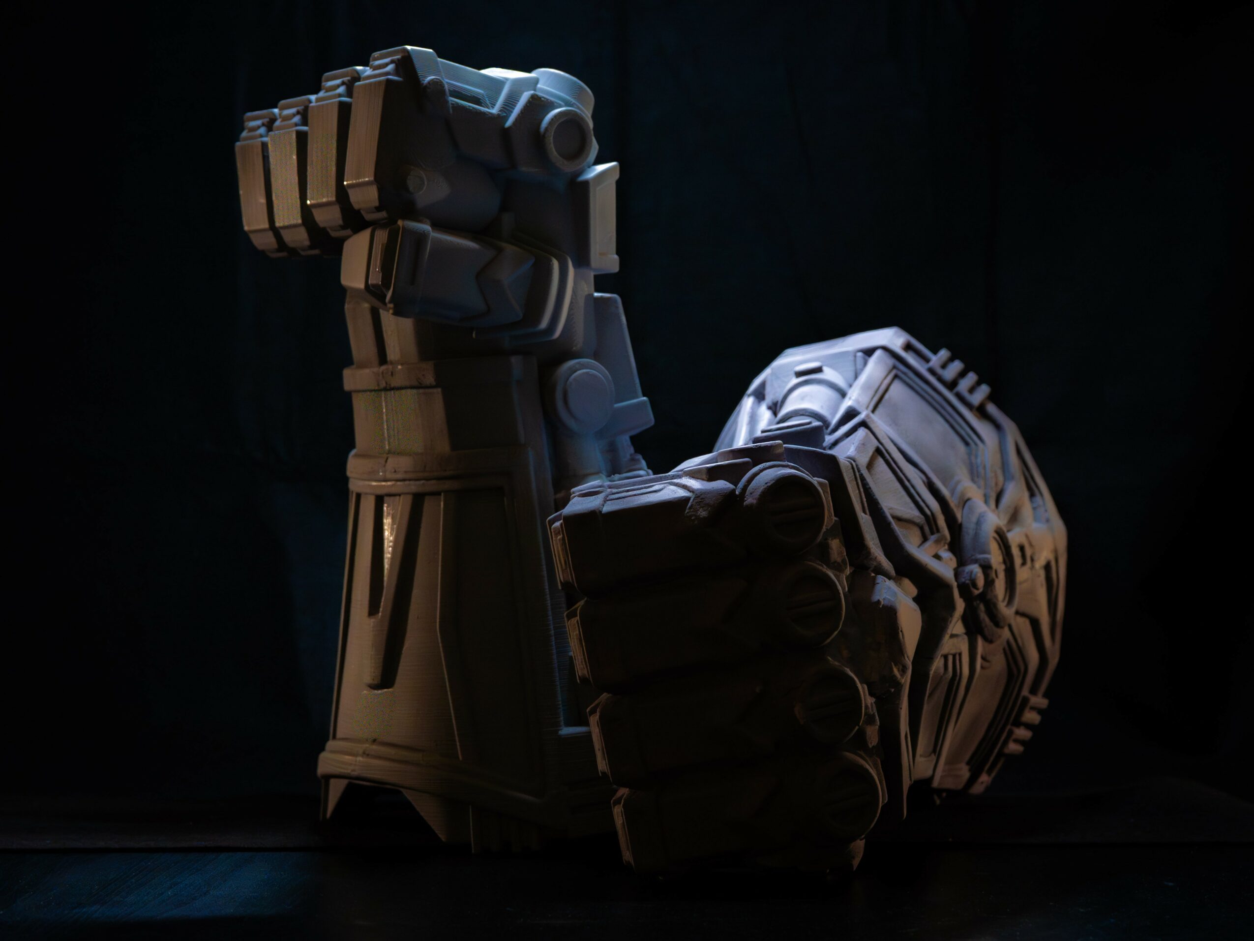 A robotic arm and fist made of dark metal, illuminated against a dark background.