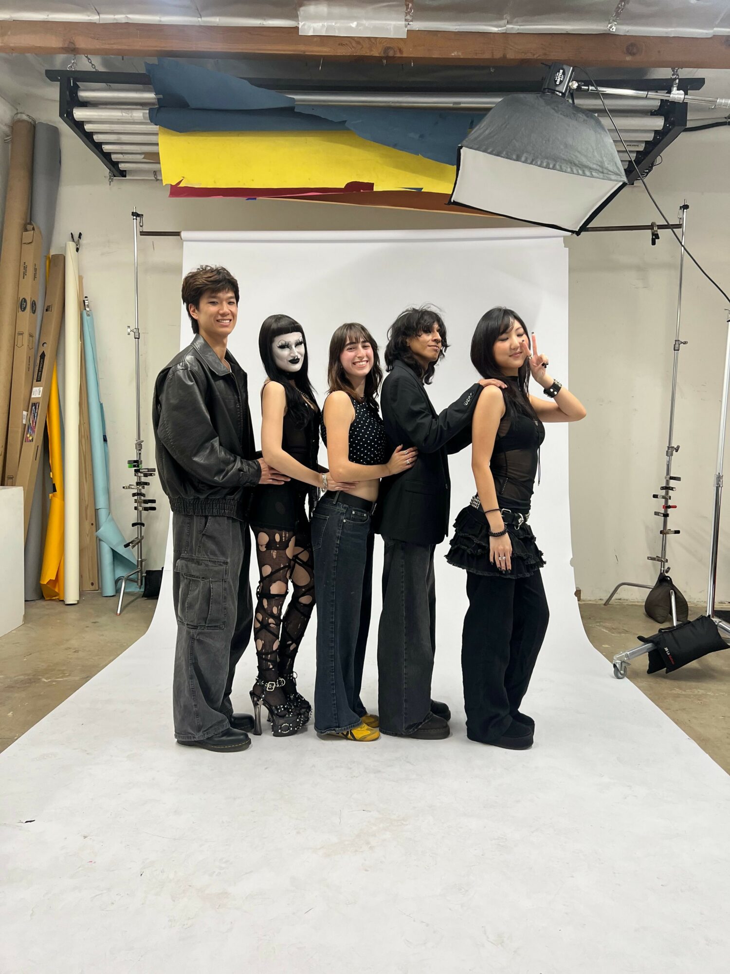 Group of five people posing in a photography studio with equipment and a white backdrop.