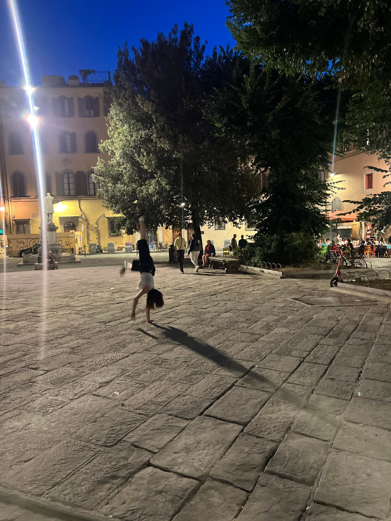 Child walking on a paved street with trees and buildings in the background during evening.
