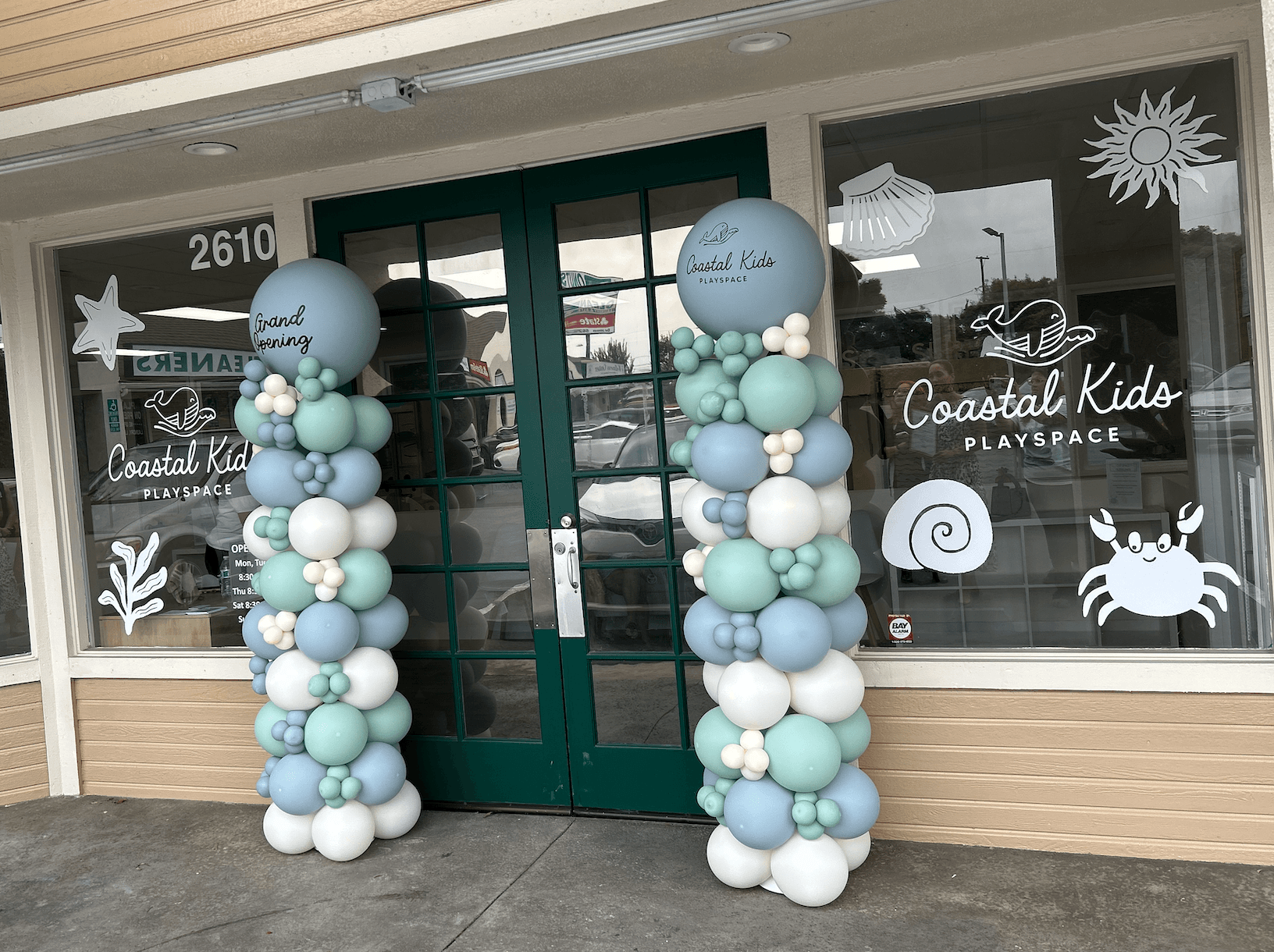 Decorative balloon columns with pastel blue, white, and gray balloons outside Coastal Kids Playplace entrance.