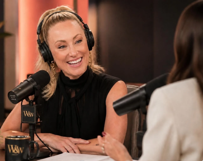 Woman with blonde hair wearing headphones, smiling, speaking into a microphone during a recording session.