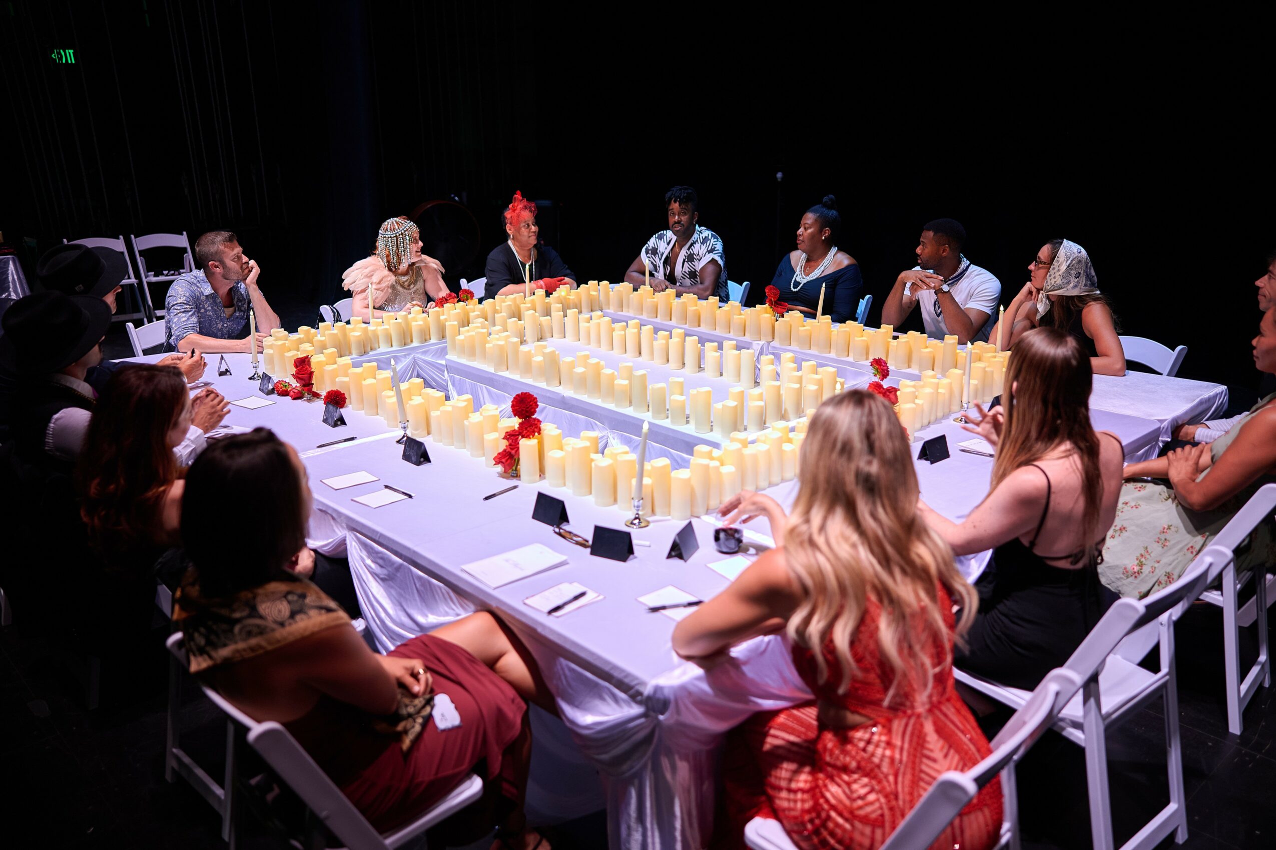 People seated around a large rectangular table with yellow and red decorations, in a dark room, engaging in a discussion.