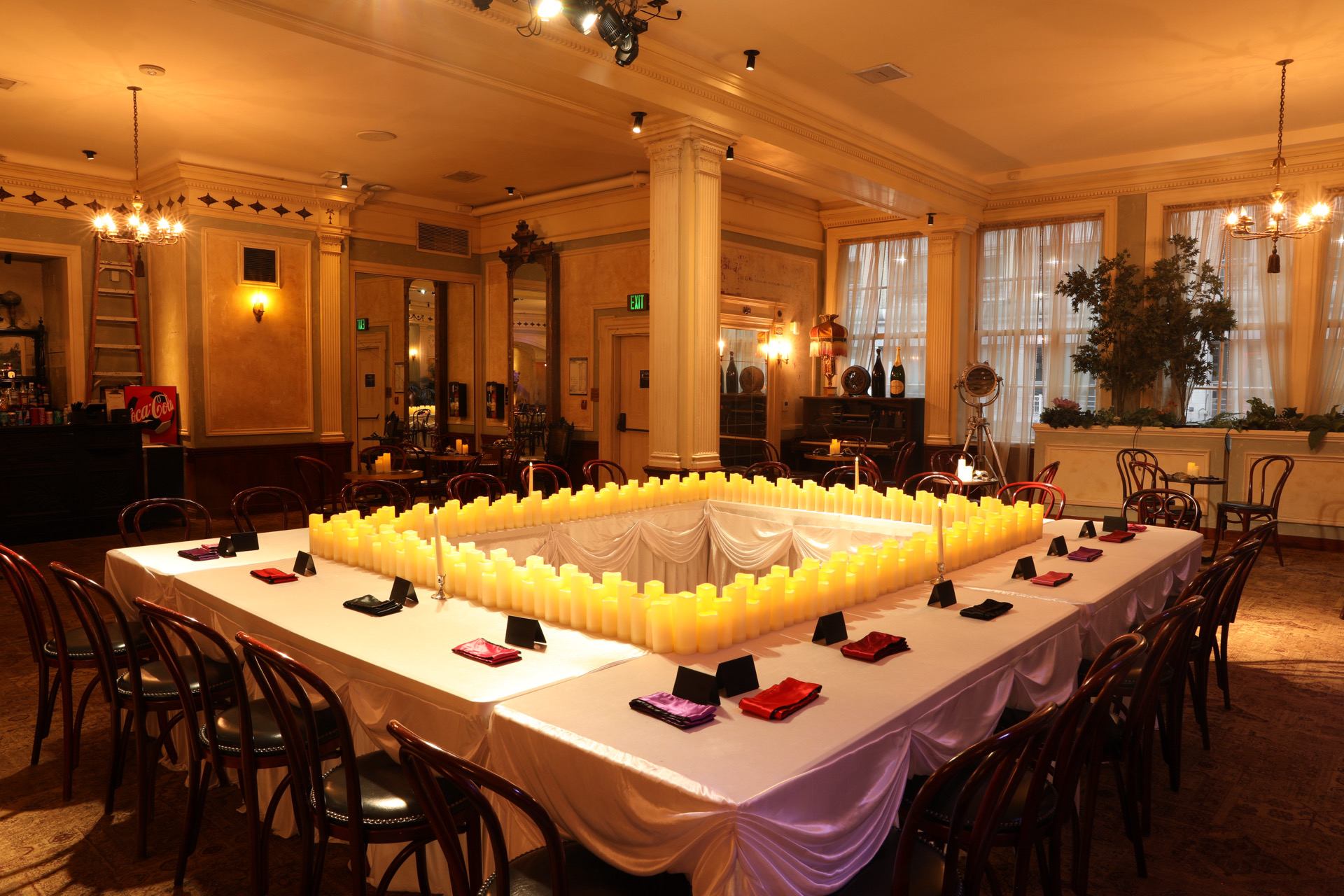 Elegant dining room with a large table decorated with candles, surrounded by chairs, and large windows with curtains.