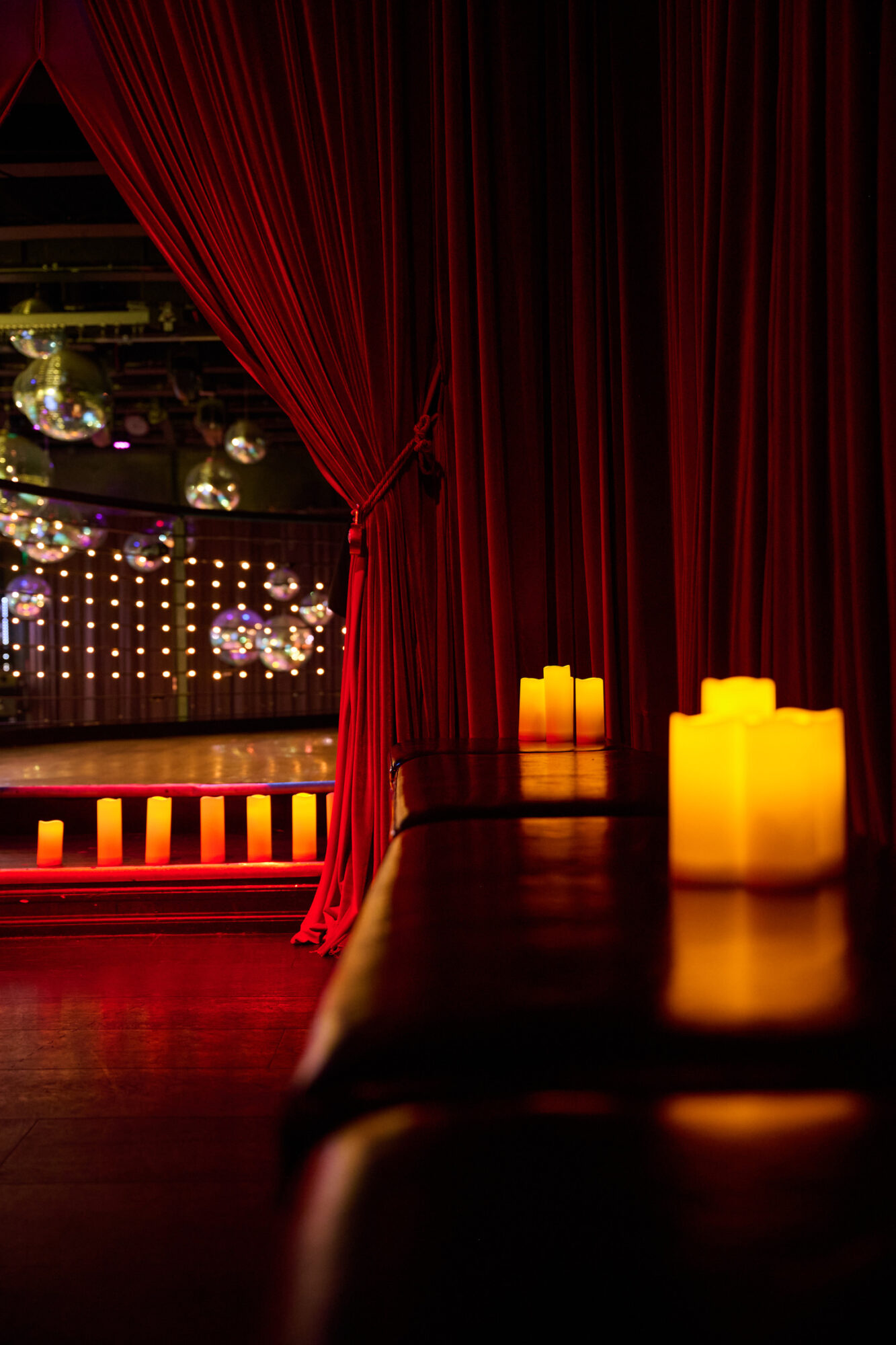 Stage with red curtains, candles on table, and a lit-up background with hanging lights and disco balls.