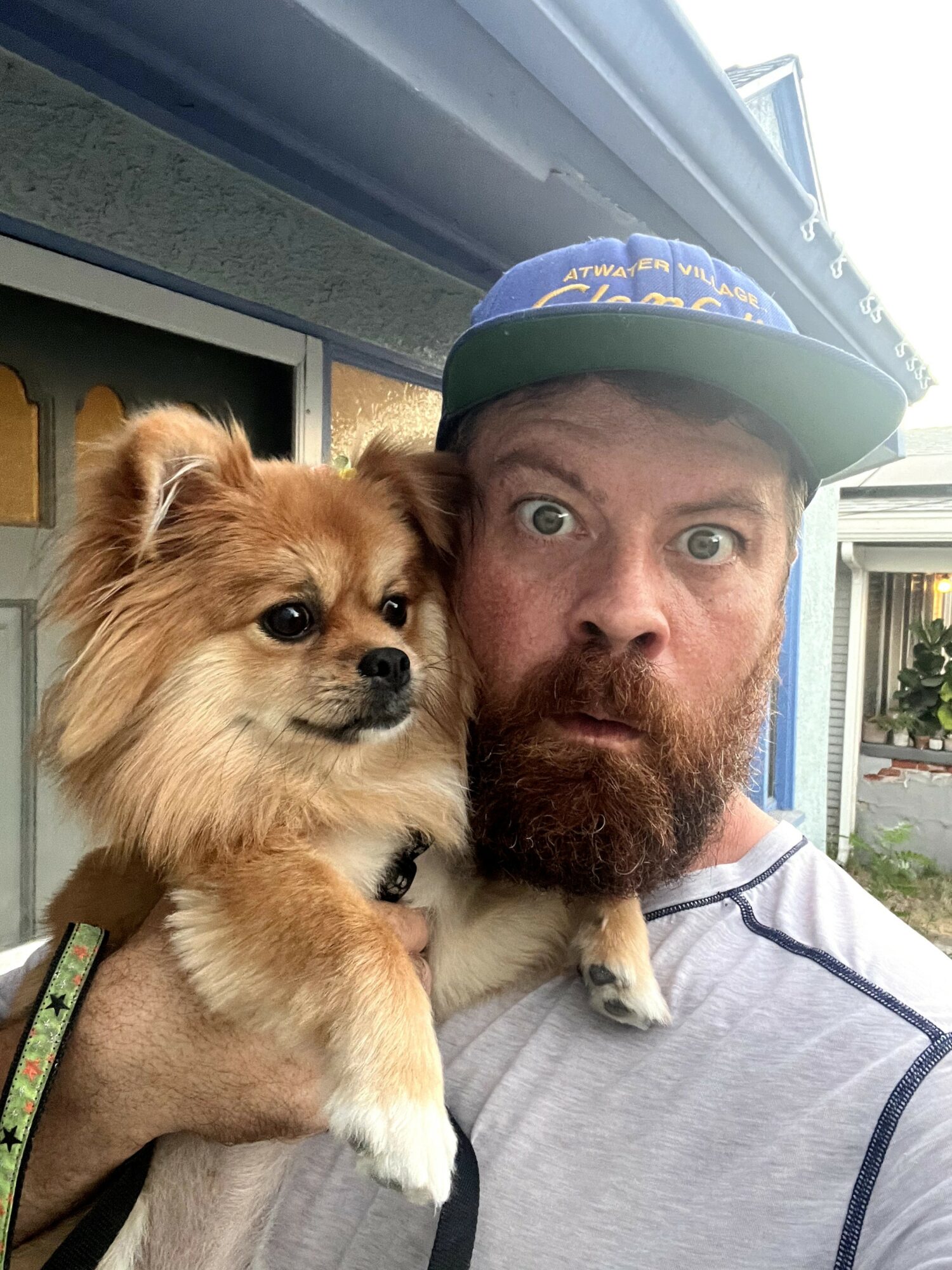 Man with a beard holding a small fluffy dog outdoors, both looking at the camera.