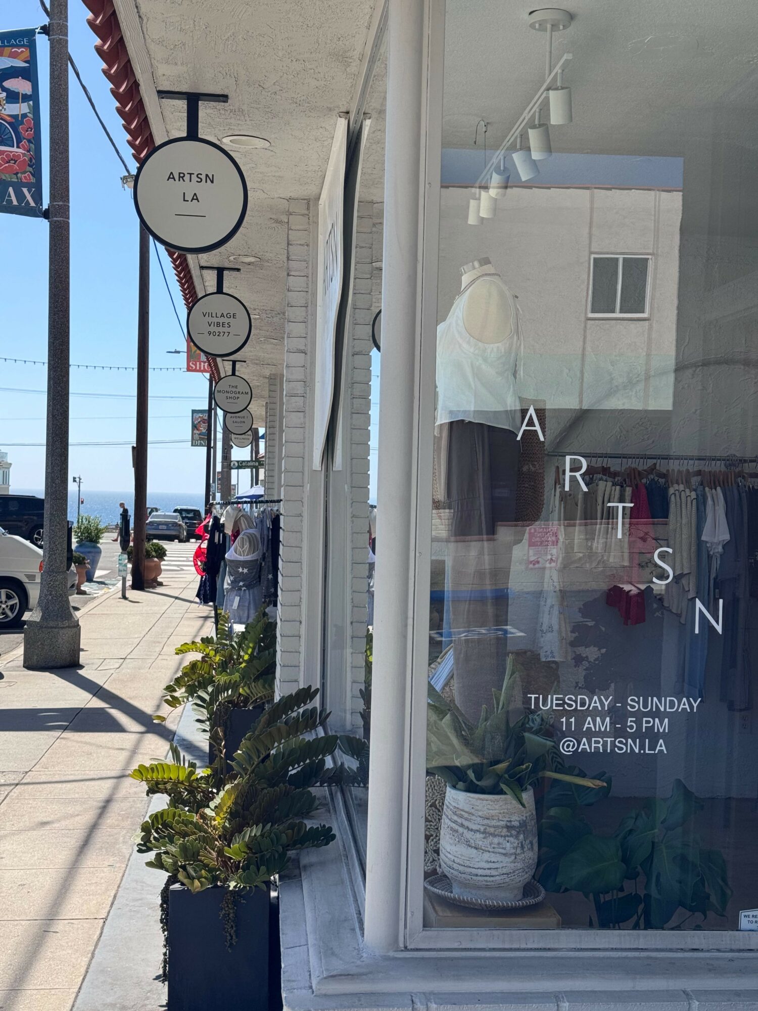 Store window with clothing display, sidewalk with signs and people, and a building in the background.