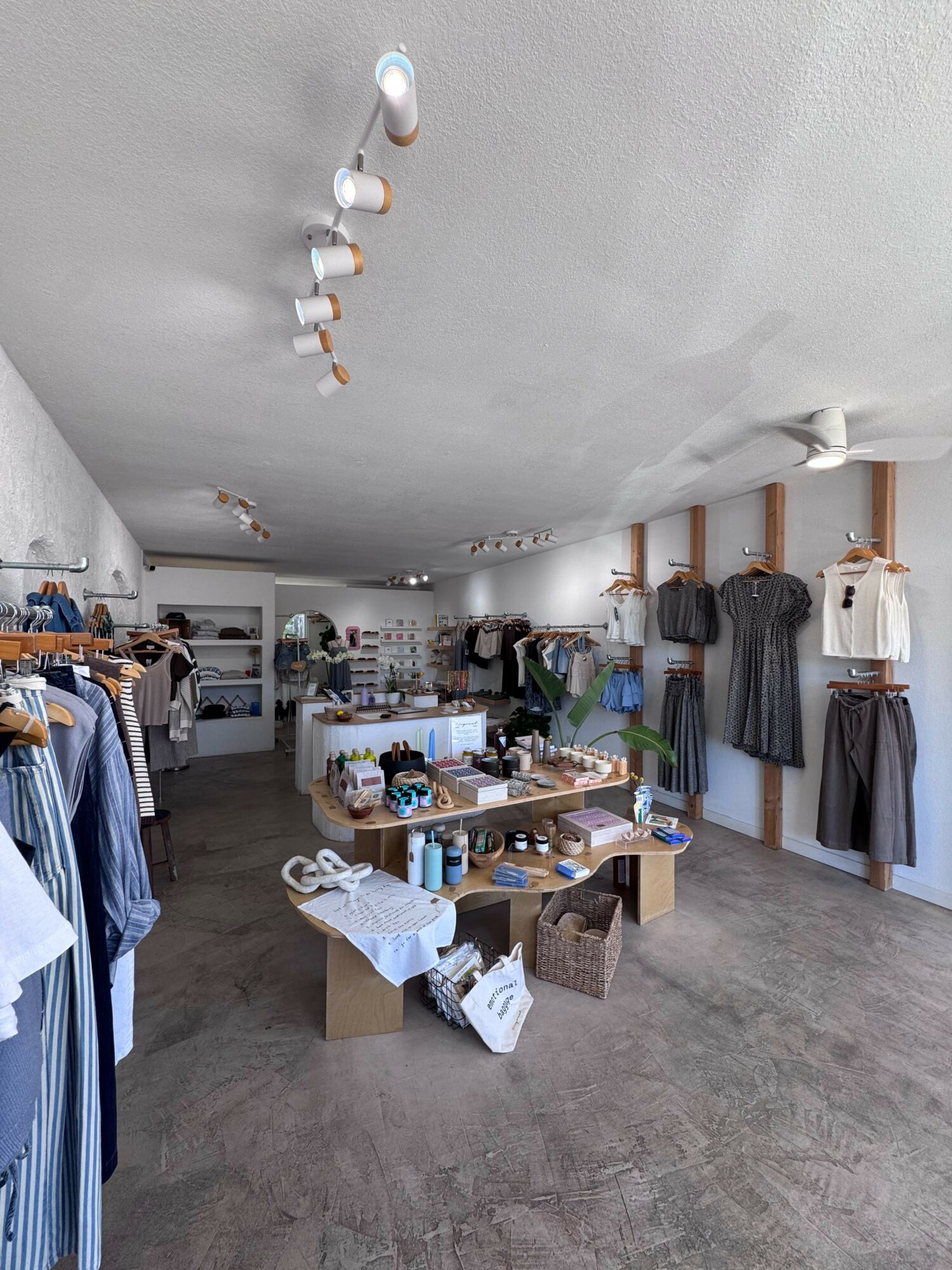 Clothing store interior with racks, shelves, and tables displaying clothes and accessories, well-lit and organized space.