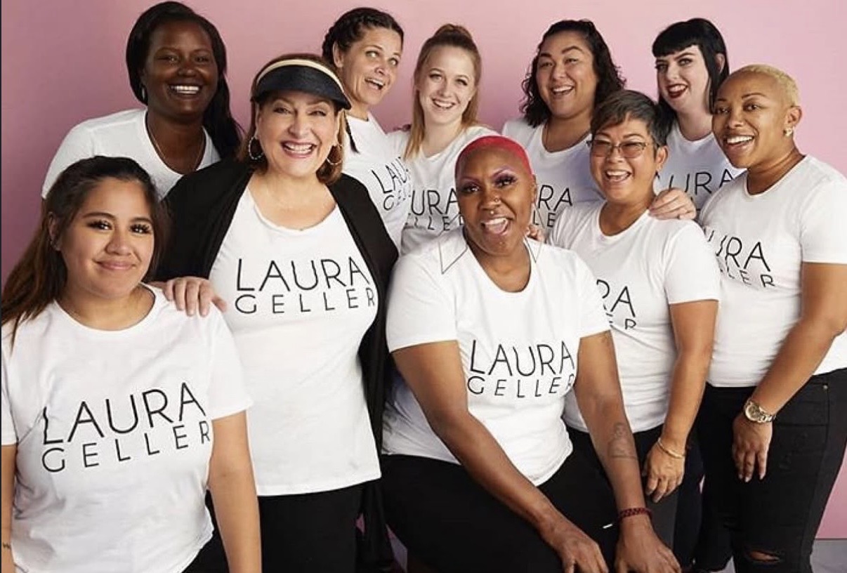 Group of diverse women smiling, wearing white T-shirts with 'LAURA GELLER' text, standing against a pink background.