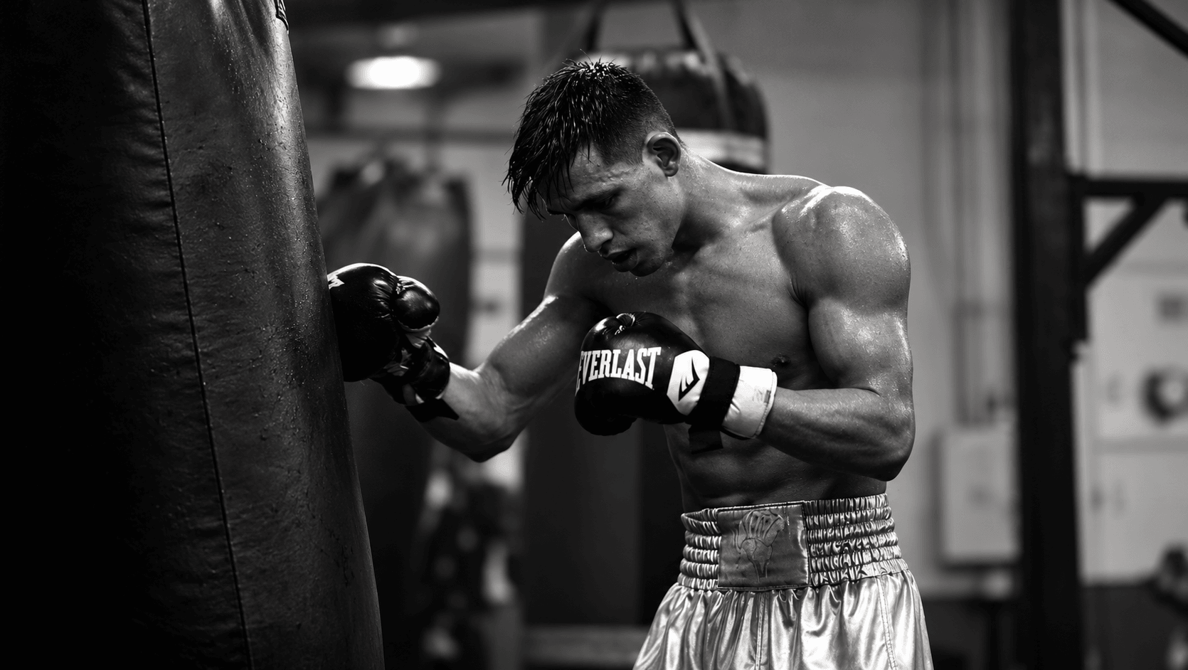 Young male boxer in gloves and shorts hits a punching bag in a gym.