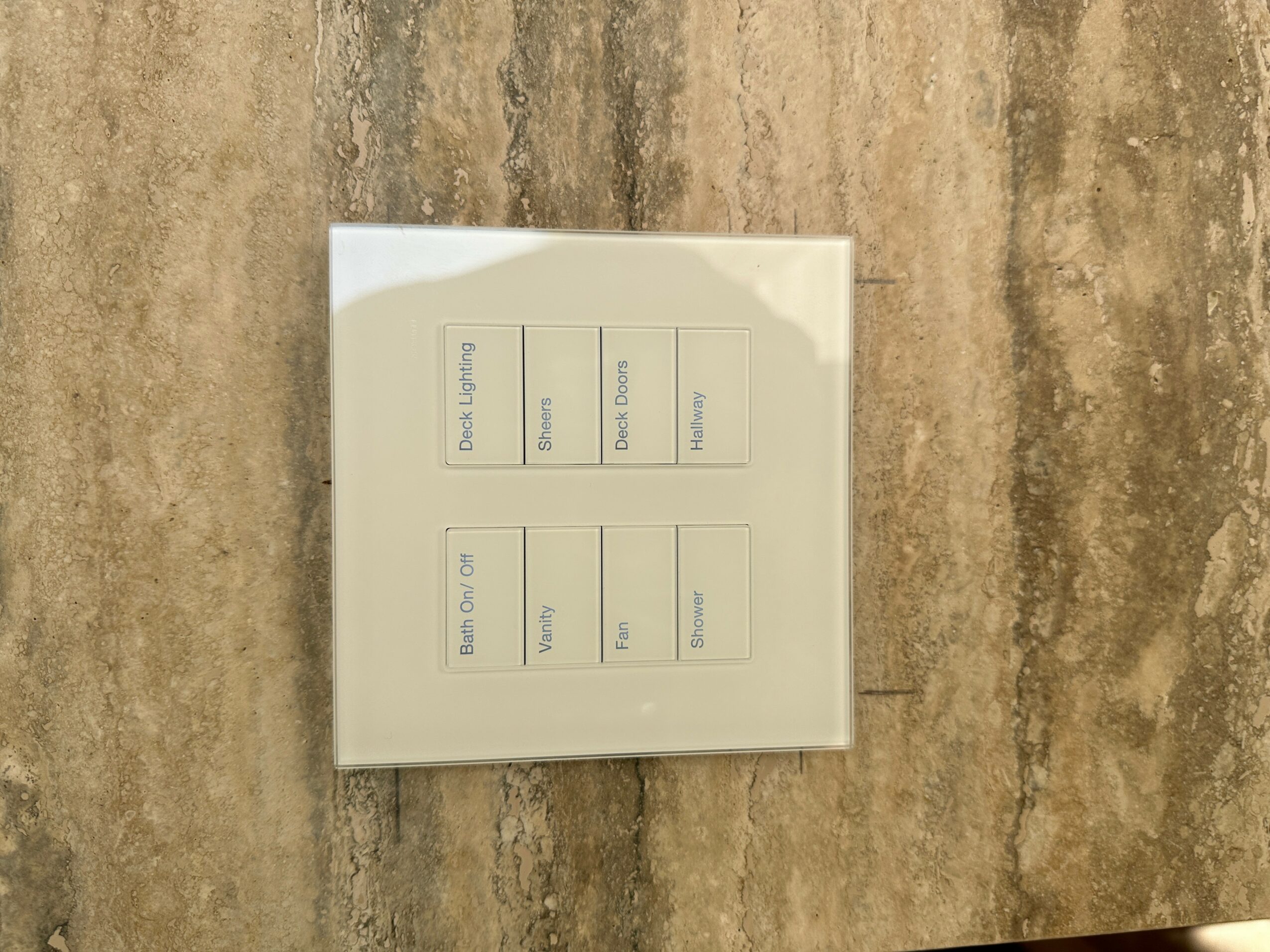 A white control panel with buttons and labels on a textured beige surface.