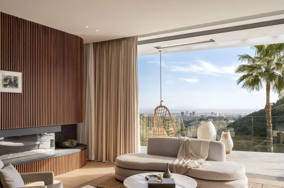 Living room with large window, view of trees and sky, white sofa, round coffee table, and wooden wall paneling.