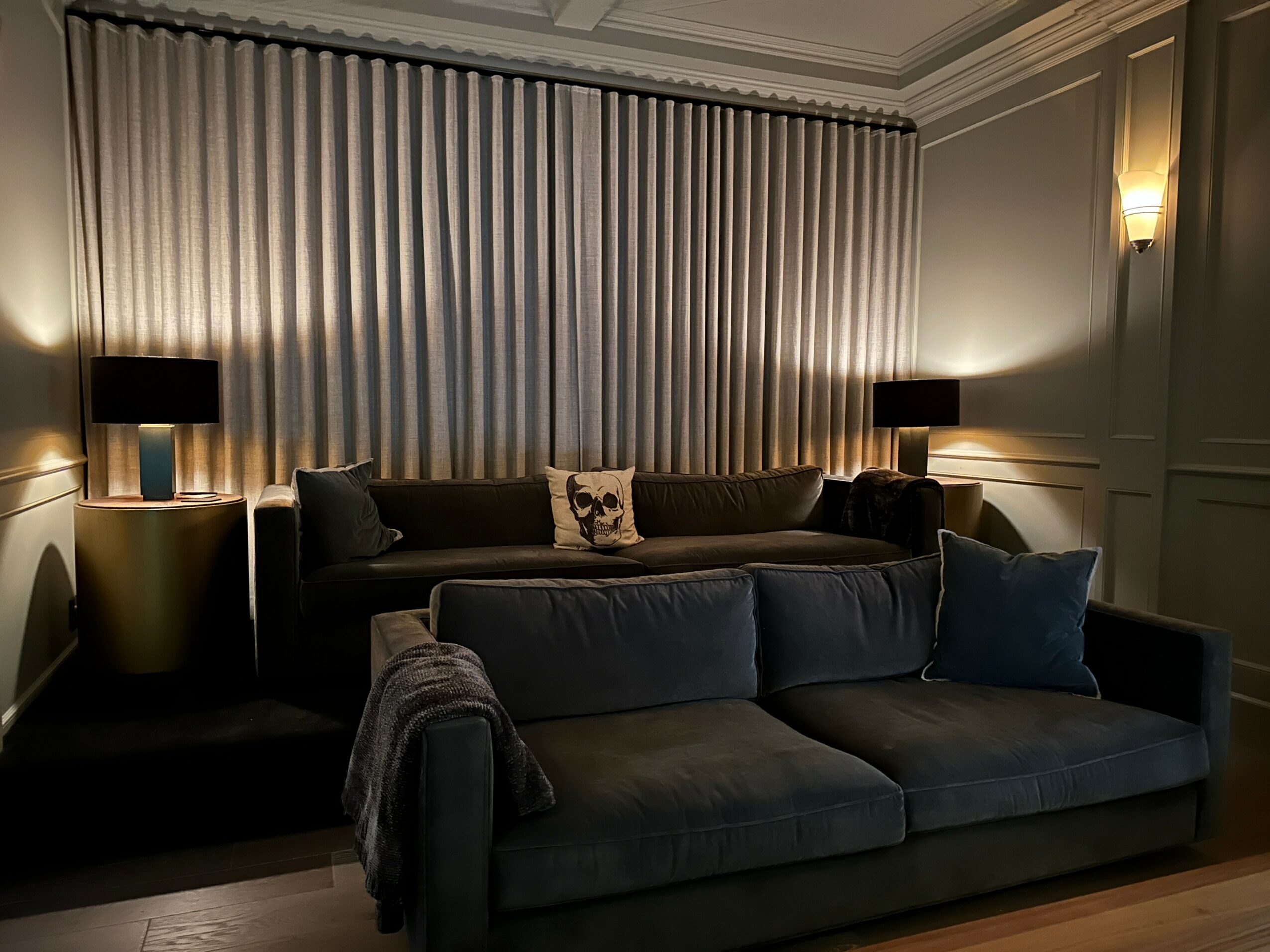 Living room with two sofas, curtains, and lamps on side tables, dimly lit with warm lighting.
