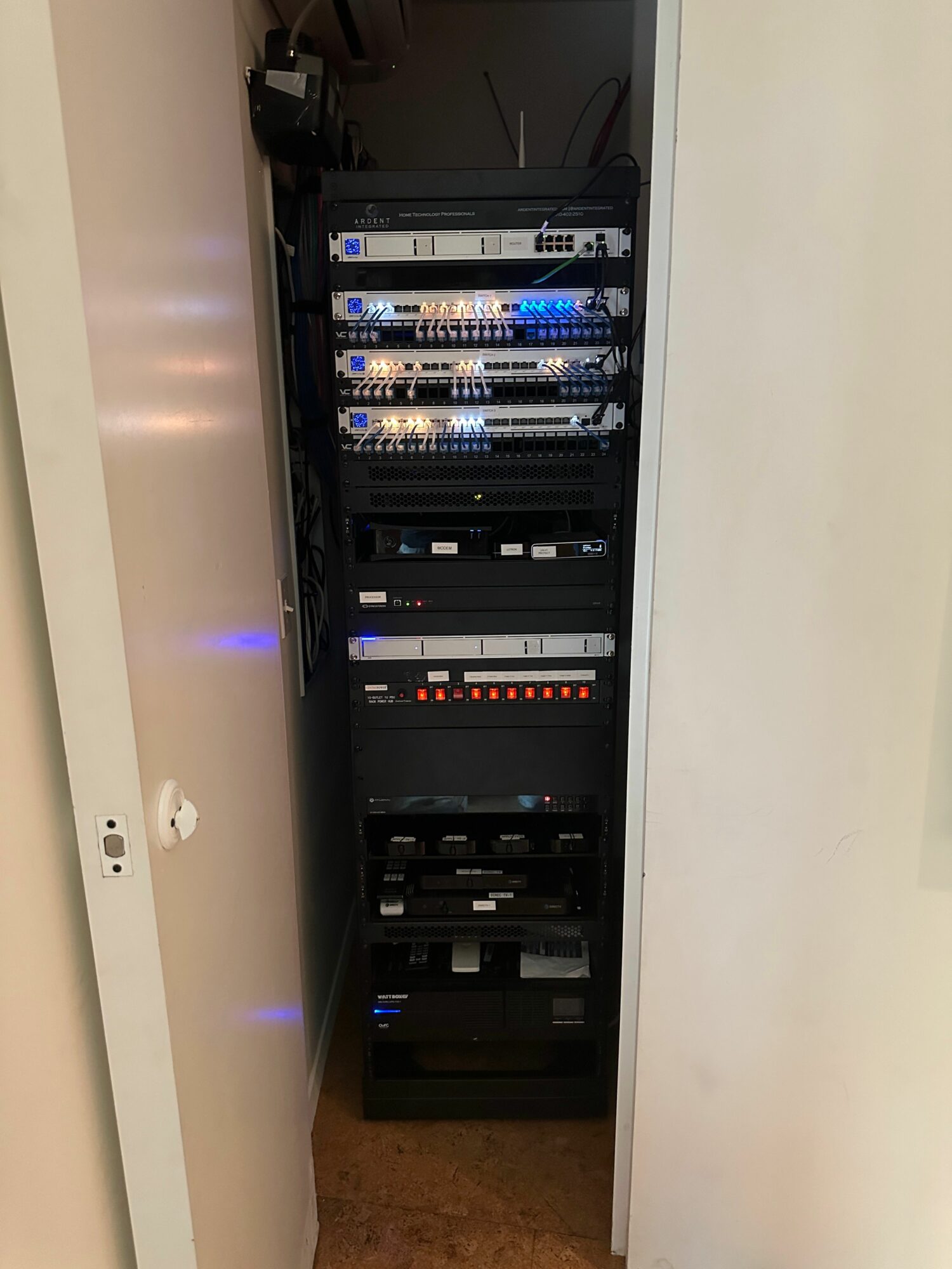 Server rack with multiple electronic components and blue LED lights, viewed from the side, inside a white cabinet.
