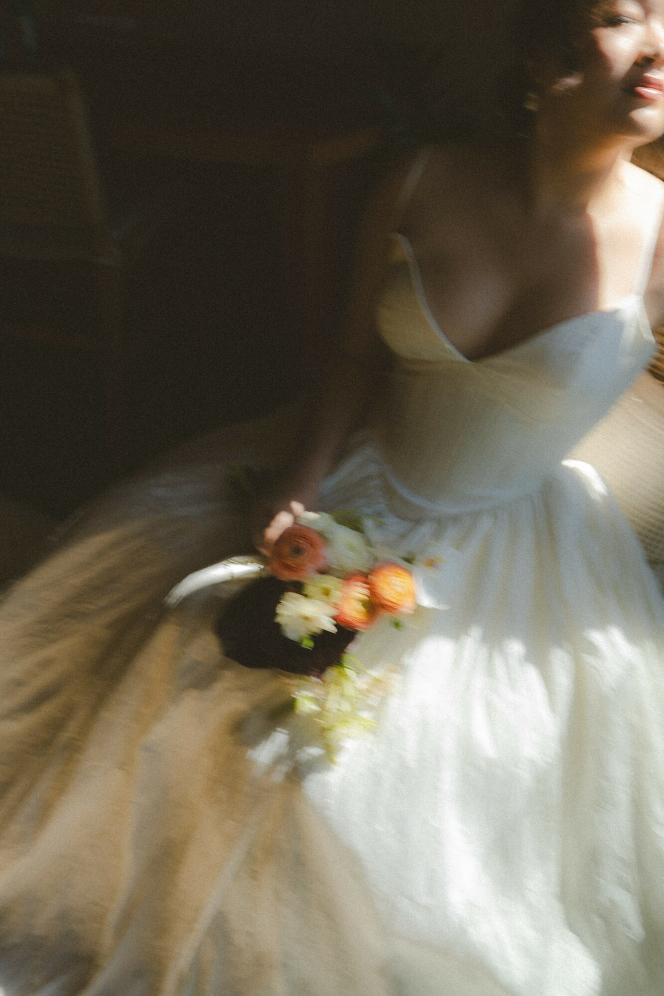 A woman in a white dress holding a bouquet of flowers, sitting in a dimly lit room.