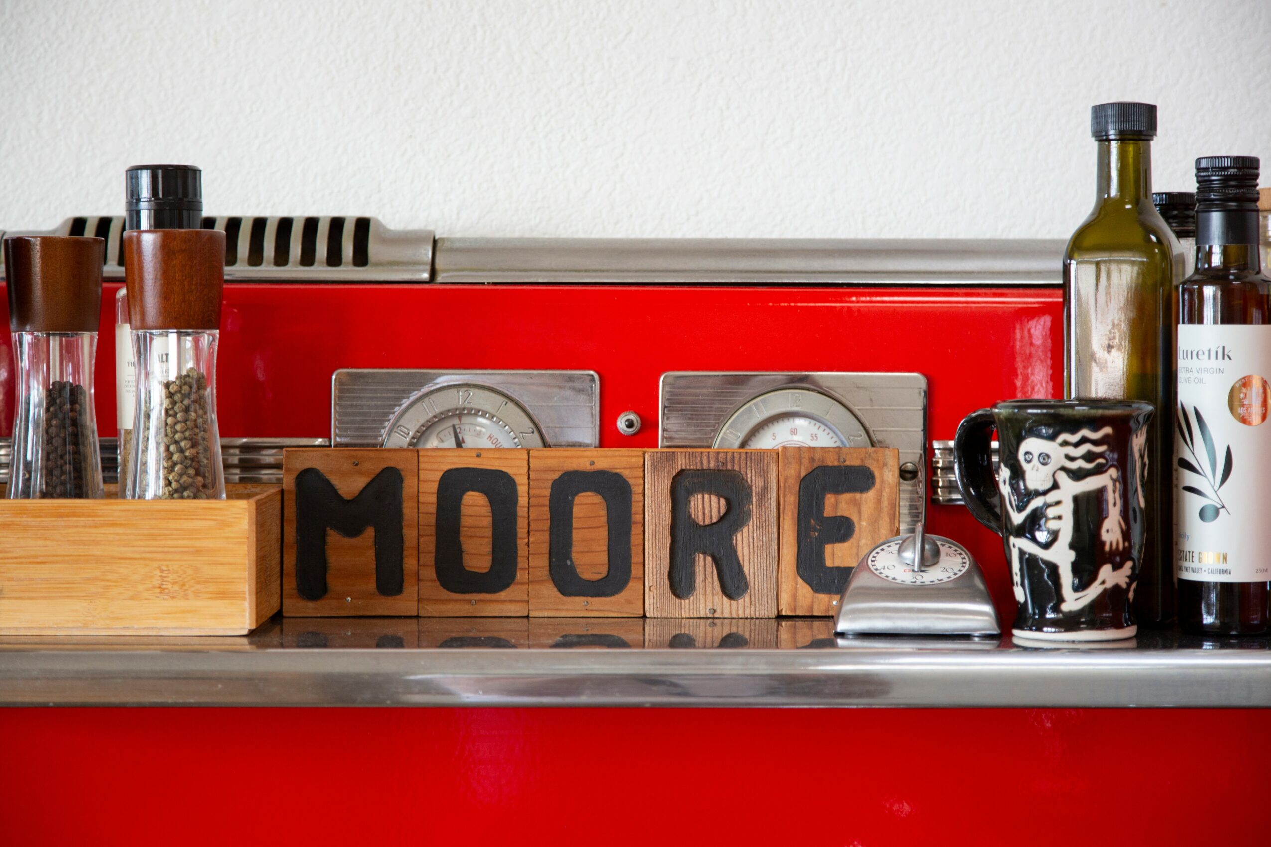 Kitchen shelf with spices, bottles, a radio, and a mug with a skeleton design, spelling 'MOORE' in wooden blocks.